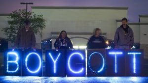 Några människor står bakom stora lysande bokstäver i blått som säger Boycott.